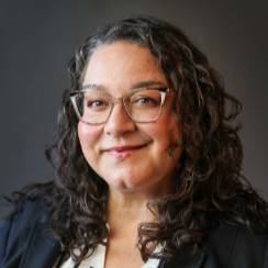 Hedge shot of Jamie Yesh wearing a black jacket and black and white striped blouse.