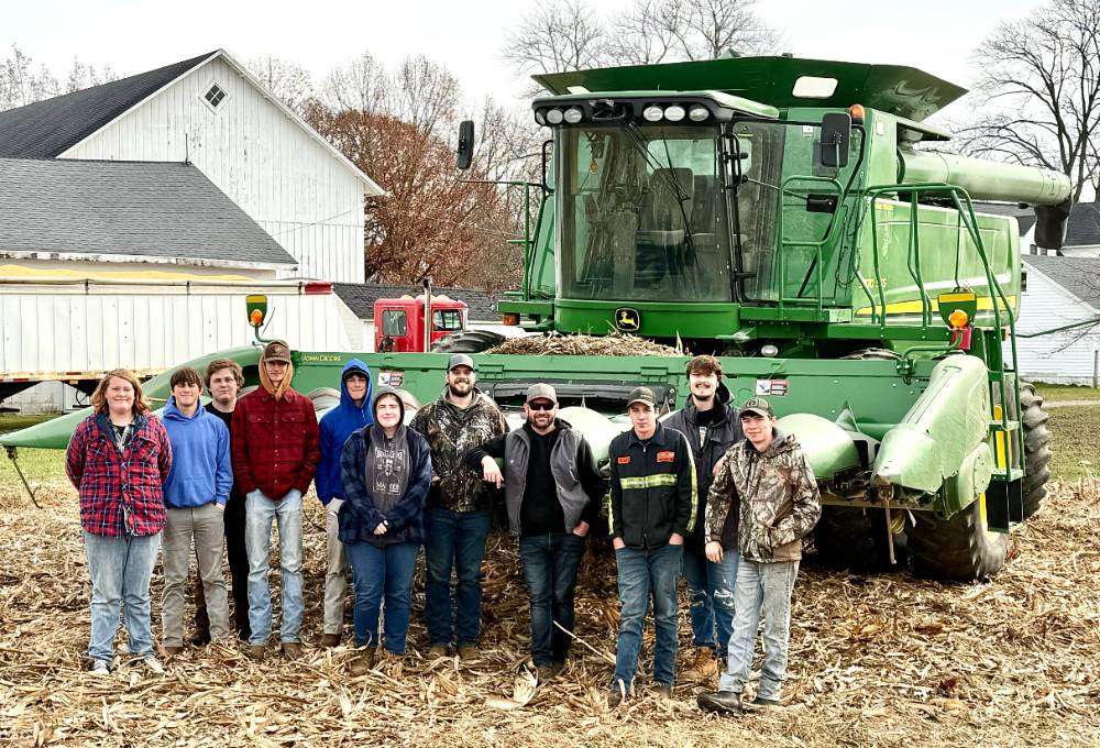 Agriculture class standing on farm in front of green combine