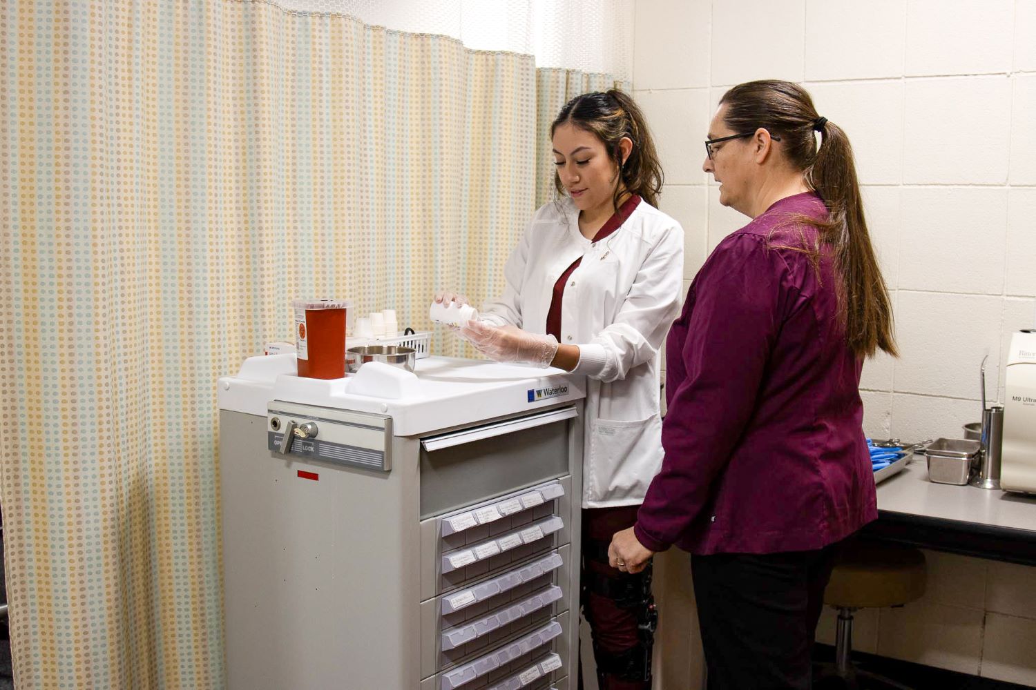 Instructor reviewing medication as they stand over a cart.