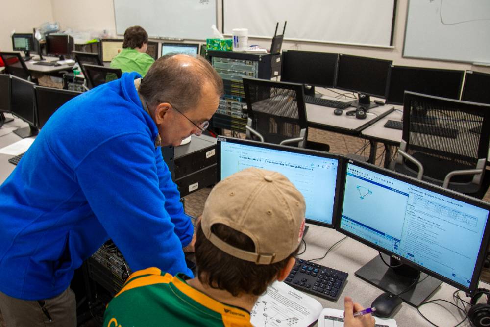 Instructor standing over student, helping him work on his project in class