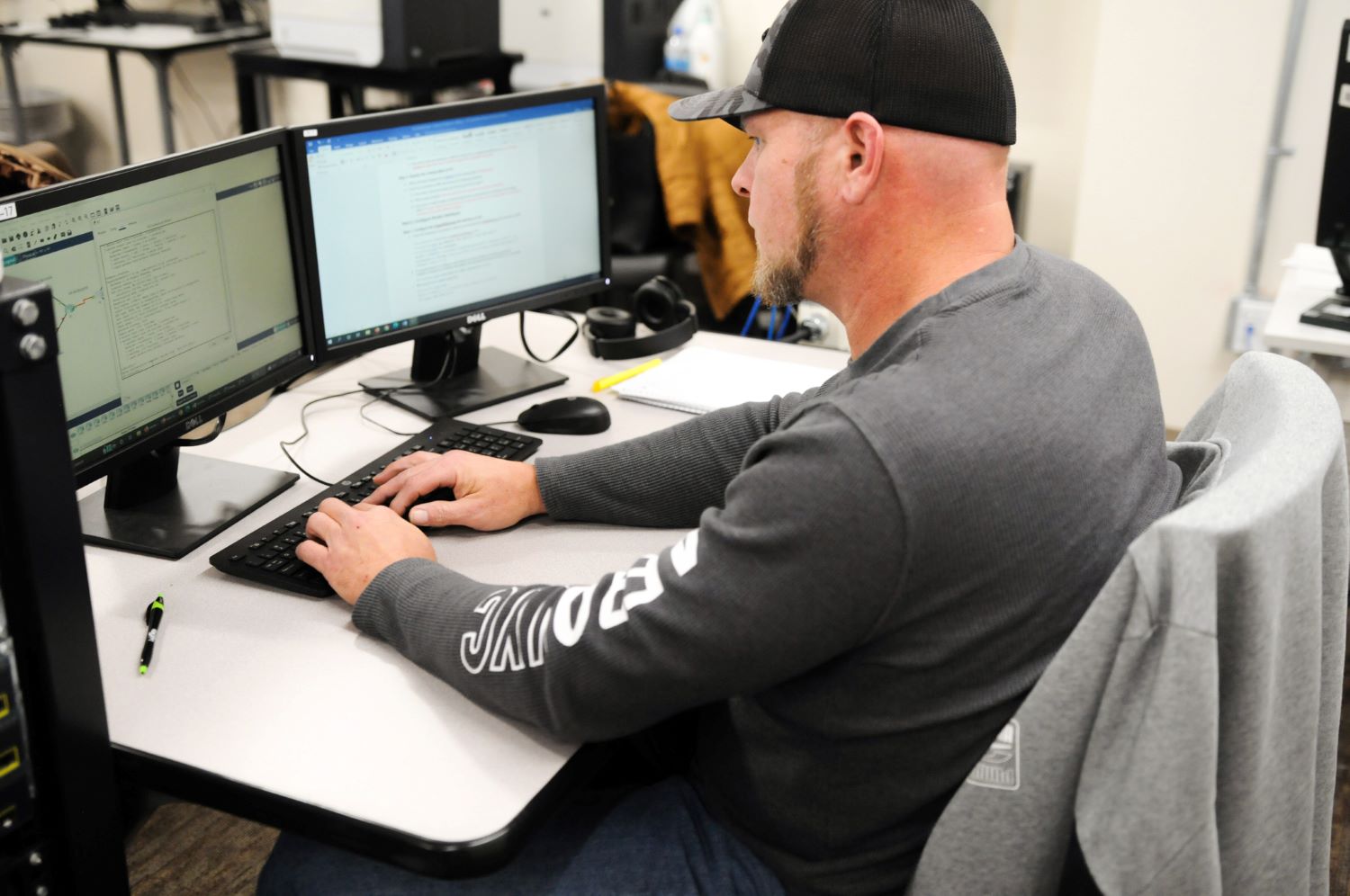 Computer student sitting at a bank of three monitors and typing on a keyboard