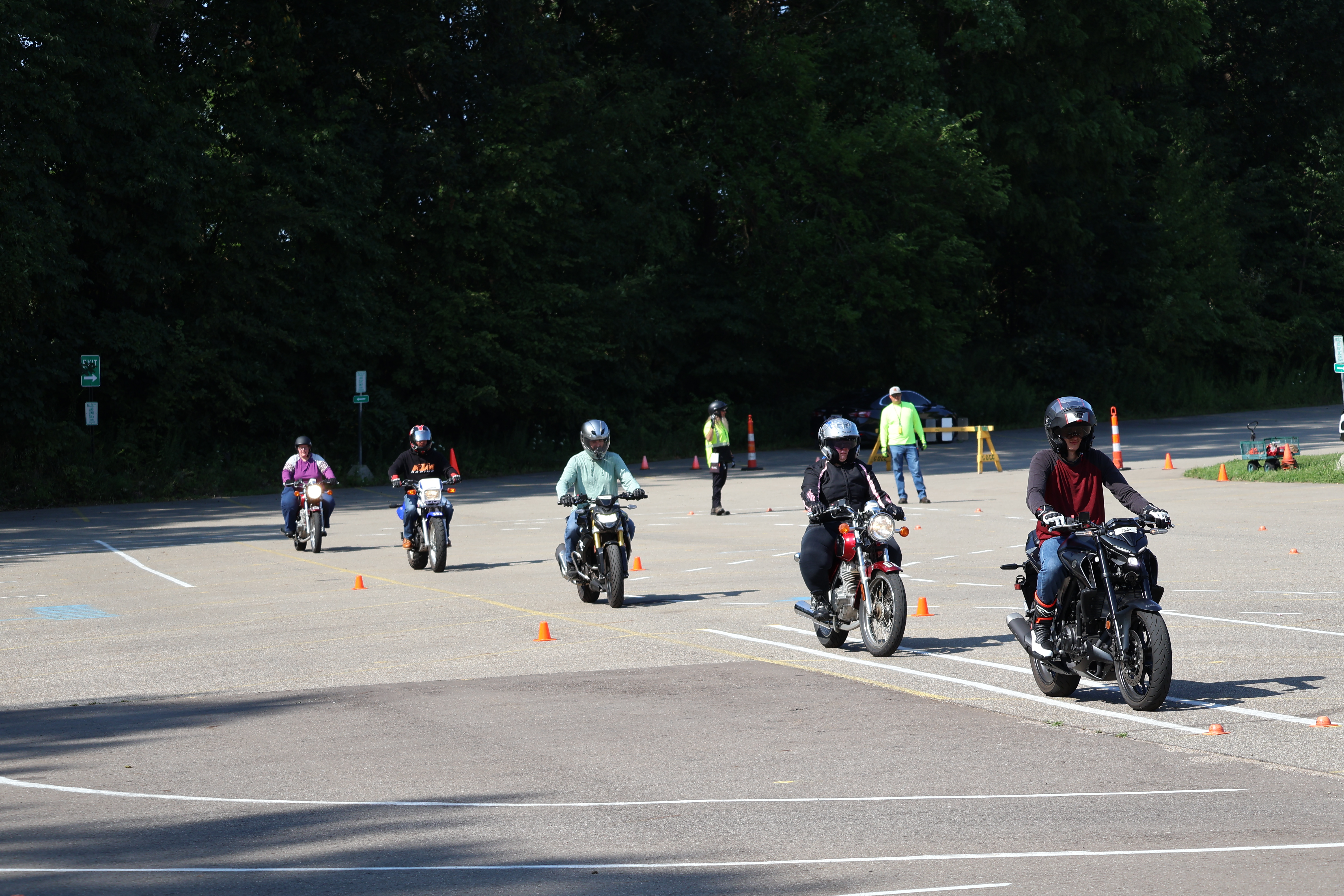 five people riding motorcycles in parking lot with instructors