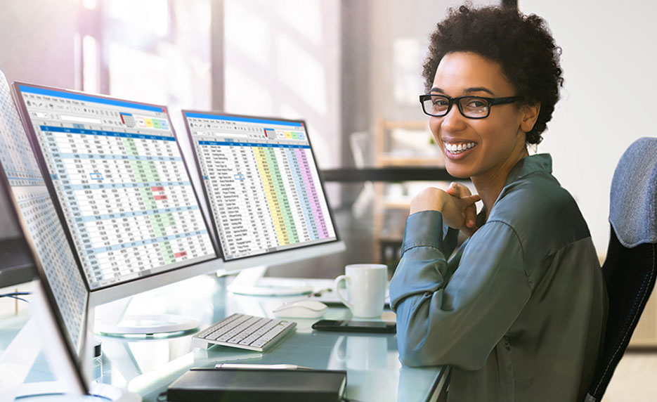 Female in front of two computer screens looking at data 