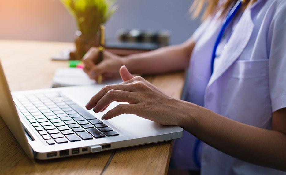 Woman in scrubs sitting at laptop punching keys