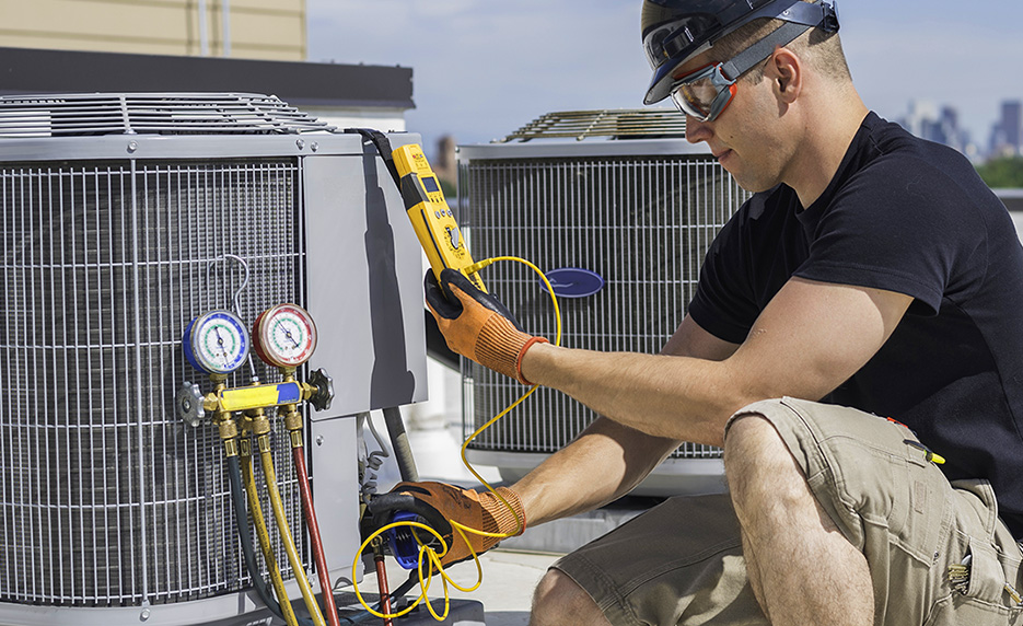 Man crouching down with measuring device, measuring coolant in an air conditioning unit