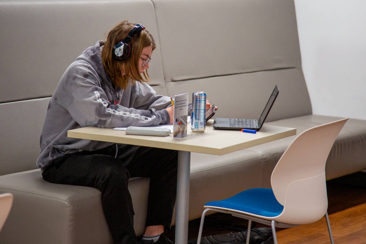 student wearing hoodie and headphones sitting at a table in front of his laptop 