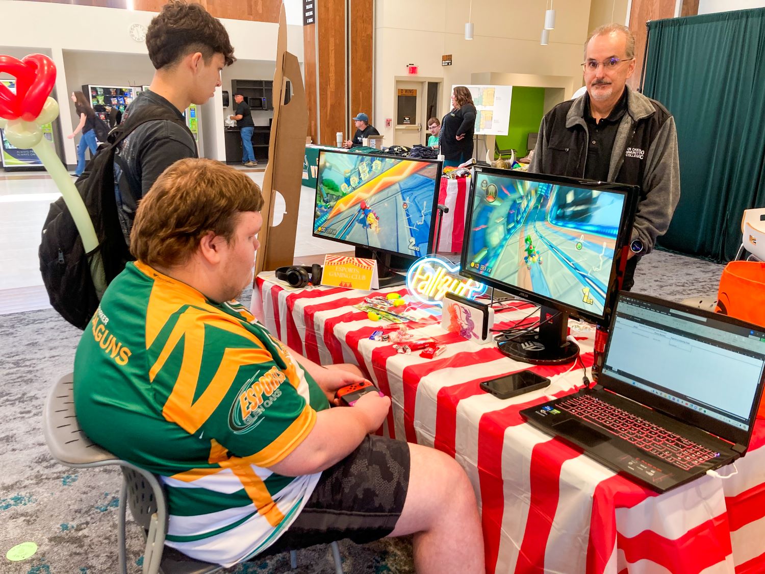 Student wearing an E-gaming jersey, seated at a table in front of a computer, playing games.