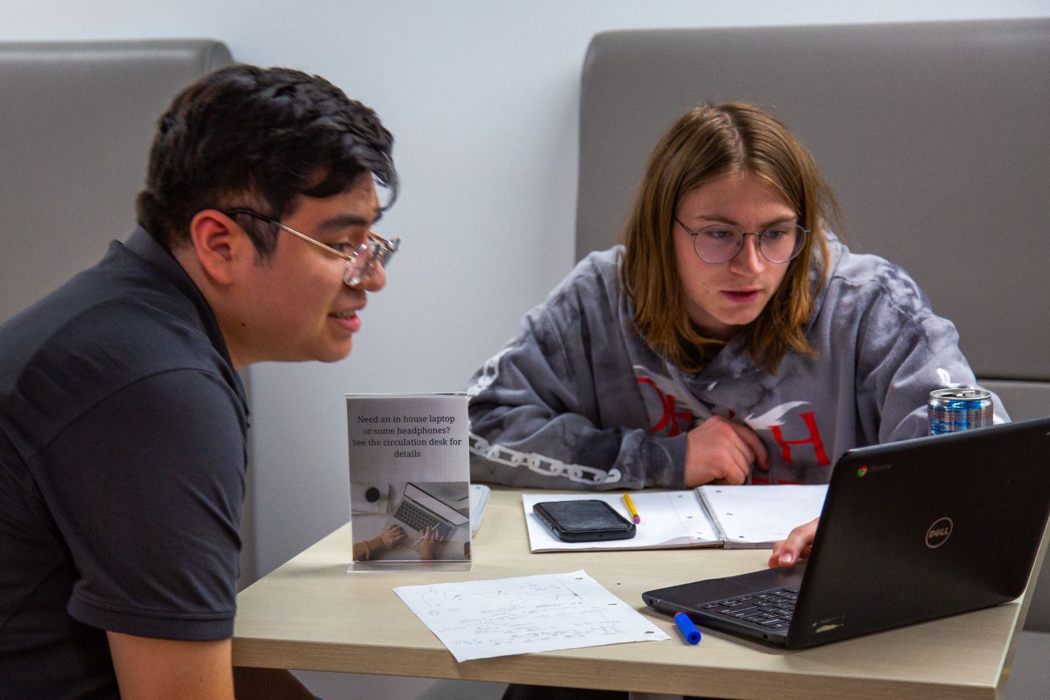 two male students sitting at a table looking at a laptop together