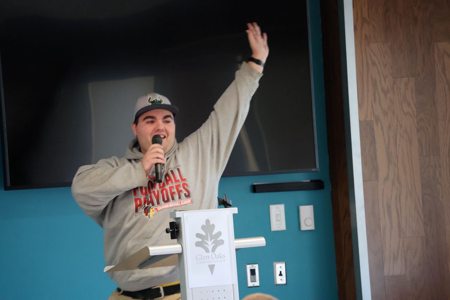 Male college student standing at podium holding a microphone and raising his left arm high.