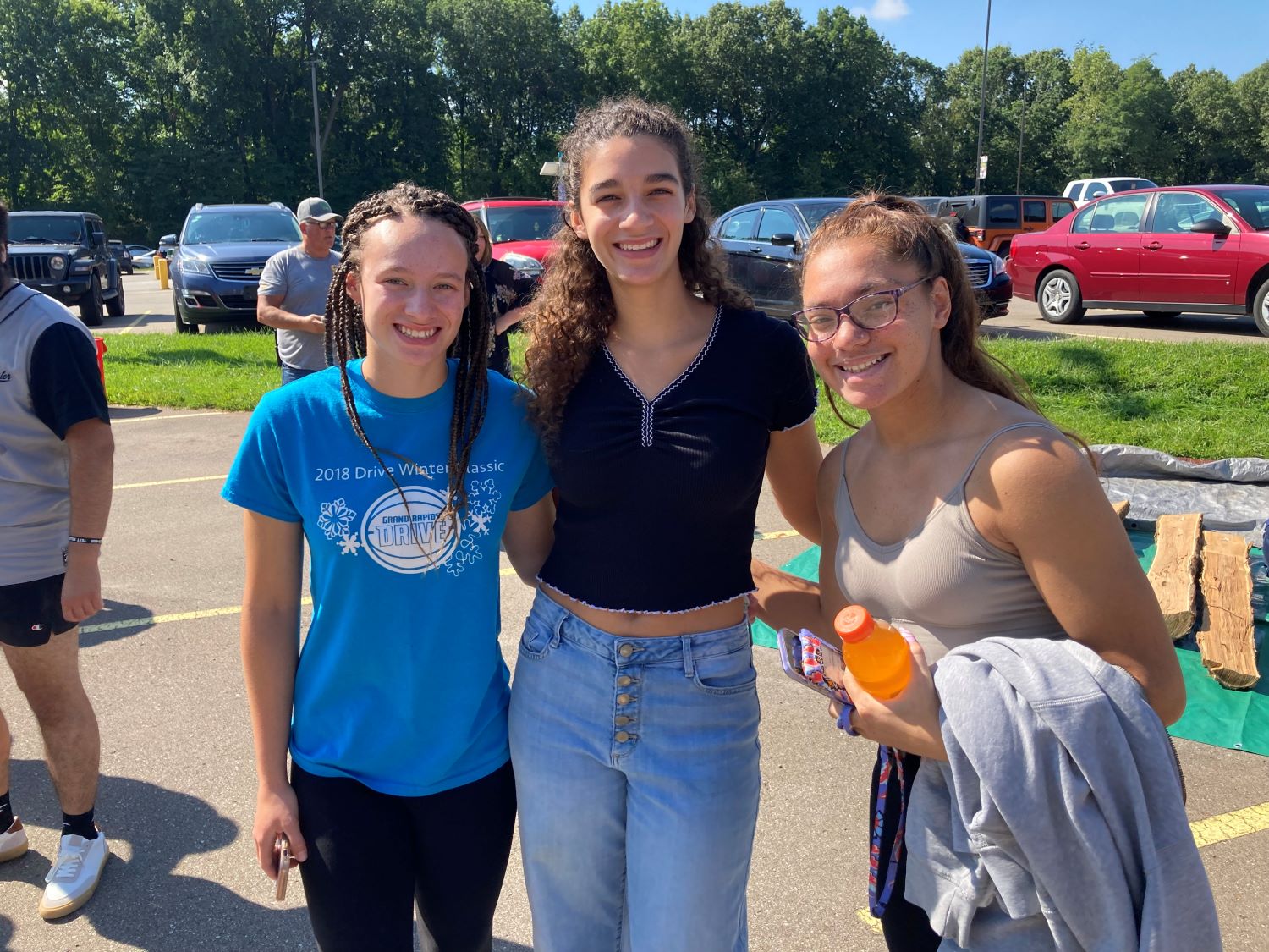 Three female students standing arm-in-arm in parking lot